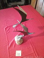 Front and side view of the brass seagull bird sculpture on quartz rock shown on a red cloth.