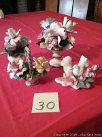 Four vintage Capodimonte porcelain figurines displayed on a red cloth: three floral and one bird decoration