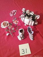 Front view of six Capodimonte porcelain figurines including metal stem roses, barrel vase, purple shoe, and old car on red cloth.