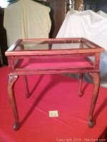Front view of the wooden display cabinet/end table showing the glass top and wood legs, placed on a red cloth.