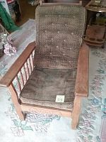 Front view of antique Morris chair with cushioned seat and back, wooden frame with spindled sides, and carved apron.