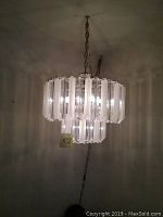 Full view of chandelier showing two tiers of clear and frosted vertical Lucite panels and metal frame with chain.