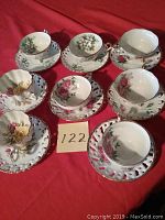 Eight matching Cherry China tea cups and saucers set with painted floral designs in multiple colors displayed on red background, showing top and angled views.