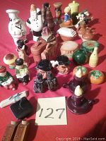 Overview of multiple vintage salt and pepper shakers arranged on a surface showing various figurines, fruit, and chef shapes.