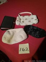 Four vintage purses on a red surface: three beaded purses (two white, one black) and one black sateen purse with hard frame.