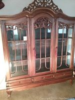 Full view of the carved wood china cabinet with glass doors and carved details.