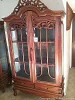 Front view of the carved wood china cabinet showing detailed glass panel doors, two drawers, and carved wood trim.