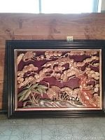 Full view of the framed wood relief, showing cranes and trees scene with red background and black frame.