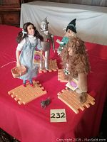 All four Wizard of Oz dolls positioned on interlocking yellow brick road sections with small Toto figurine in front.