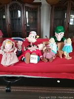 Full lot of 11 vintage character plush and dolls on red cloth with dark wood background.