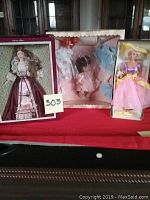 Photo of three dolls: Victorian Barbie Collector Edition boxed doll, Tiny Tears doll with two dresses in box, and Barbie doll in pink and purple outfit with yellow hat in box.