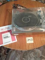 Pioneer PL-117D turntable on wooden table with cables, clear dust cover, and service manual.