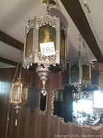 Two ornate hanging lights mounted on ceiling, decorative metalwork, amber plexiglass panels, chains for suspension.