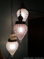 Three hanging glass pendant lights lit, showing textured glass detailing and metal fixtures. Pendant lights hang from chains.