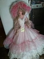 Full view of the doll showing the pink and white multi-layered dress with lace and organza skirt, large pink feather hat, and long blonde hair.