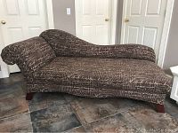 Full view of the chaise lounge sofa showing medium brown upholstery with tan script pattern and wooden legs.