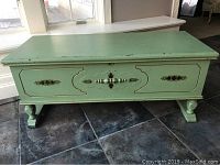 Front view of vintage minty sage green Lane cedar chest with gold decorative accents, showing top, front panel, and feet on tile floor.
