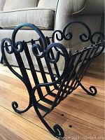 Full view of the wrought iron magazine rack highlighting the scrolled decorative sides and horizontal iron bars on the back and bottom.