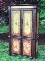 Full front view of the floral accent TV armoire outdoors, showing overall condition and painted floral designs on the doors.