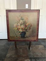 Frontal photo of the folding card table showing full floral artwork on the tabletop with legs folded.