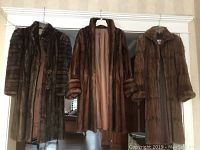 Photo of three vintage long fur coats hanging on a white door, showing front views and fur textures