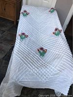 Full view of white chenille bedspread draped to show floral bouquet clusters and textured linear pattern.