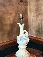 Front view of the porcelain figural cherub lamp showing the full lamp body with pastel pink and mint green tones, including cherub faces and floral decorations.