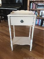 Front view of shabby chic side table with turned legs and drawer with decorative metal handle.