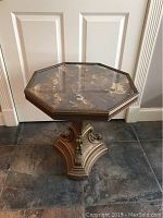 Front view of octagonal table showing glass top with patterns and scroll column base