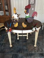 Full view of 6-piece metal garden sculpture set arranged on a round wooden table indoors, showing two flying pigs on wire stakes, a standing rooster, two small chickadees, and the spring pig.