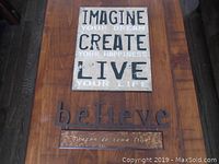 Photo showing both decorative signs laid flat on wooden surface for condition and text detail.