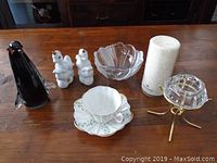 Full lot showing all items on wood table: black glass penguin, two white ceramic bird shakers, clear glass bowl, white floral tea cup and saucer, pillar candle, brass candle holder