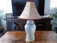 20 inch table lamp with textured clear glass base and beige with pink floral pattern fabric shade, displayed on a wooden table with a dark wood cabinet and TV in the background.