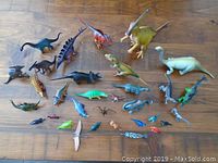 Top down view showing multiple dinosaur figures with varying sizes and colors on a wooden surface.