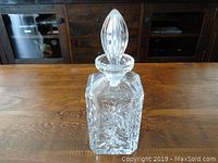 Full view of the clear crystal decanter with stopper on a wooden surface.