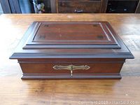 Full view of closed wooden jewelry box showing lid design and decorative keyhole plate