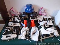 Spread of skates (roller and ice), helmets, hockey sticks, cones, and pucks on a flat surface.