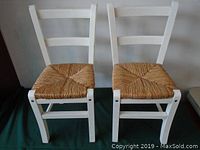 Pair of small child's chairs with white painted wooden frames and woven natural rattan seats, shown from front.
