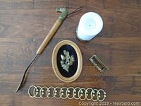 Overview image showing all items on wood surface: wooden tool with brass dog's head handle, brass rings, oval plaque with brass floral motif, brass clip, and candle.