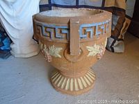 Side view of the 14-inch concrete planter showing raised ornamental grape and leaf designs and Greek key patterned band near rim with painted details.