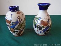 Front view of two small ceramic vases, showing detailed bird and botanical hand-painted designs with cobalt blue rims