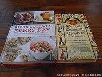 Two hard cover cook books, 'River Cottage Every Day' and 'Mennonite Community Cookbook', arranged side-by-side on a wooden surface.