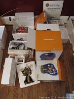Overhead view of multiple Department 56 village pieces in original boxes with foam packaging. Includes Halloween and Harley Davidson themed buildings and figurines displayed on hardwood floor.