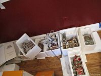 Showing multiple Dept 56 ceramic buildings arranged on floor with original Styrofoam packaging and power cords for illumination.