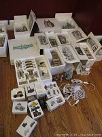 Overview of many ceramic Dept 56 Christmas in the City buildings and parts in original protective Styrofoam boxes and displayed on wooden floor.