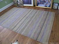 Full view of the rectangular striped area rug laid flat on hardwood floor near framed artwork leaning against walls.