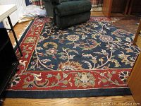 Area rug with dark blue center and red floral border, placed in living room area partly under furniture.