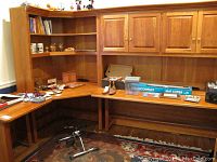 Corner of wooden desk and cabinets with assorted items including mat cutter box, shoe care supplies, and decorative pieces