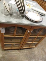 Dinnerware set displayed inside wooden cabinet shelves showing multiple plates, bowls, cups, creamer, salt and pepper shakers, platters, and serving bowls with floral and fruit pattern and silver rims.