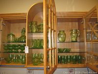 Two adjoining glass-front cabinets displaying entire green Depression glass collection across three shelves